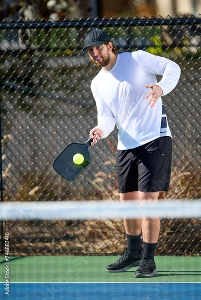 Fototapeta A man in a white shirt plays a game of pickleball in the fall