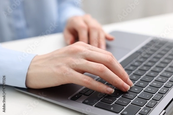 Fototapeta E-learning. Woman using laptop at white table indoors, closeup