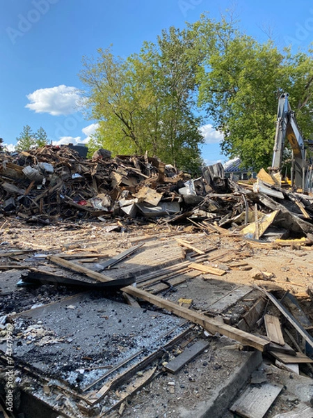 Fototapeta Remains of a building destroyed by fire. Demolition site with a bulldozer. Pile of debris after a sinister. Clean-up and rebuilding site after an incident.