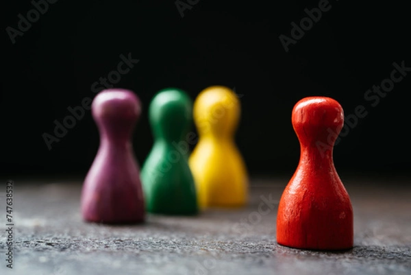 Fototapeta Three pawn-style playing pieces standing together and a red one in a distance from them