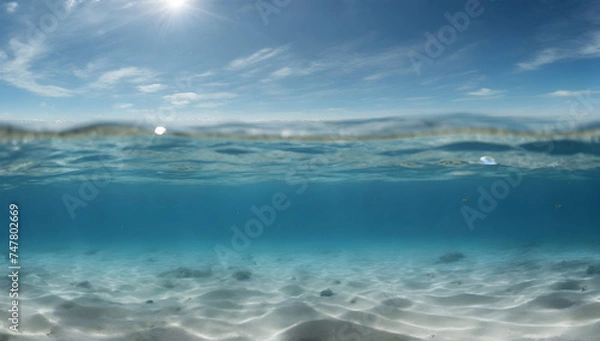 Fototapeta Blue water surface seen from underwater and rays of sunlight shining through. Underwater empty blue ocean panorama background with sandy sea bottom.