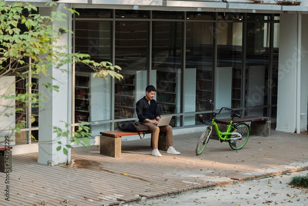 Obraz business man sitting on bench and working remotely on project with laptop