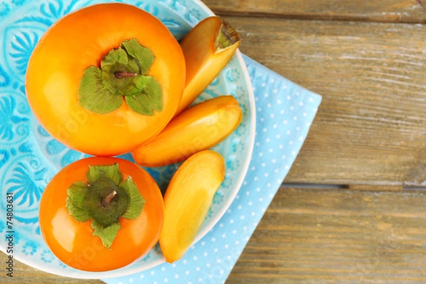 Fototapeta Ripe persimmons on plate, on wooden background