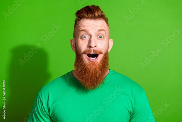 Fototapeta Photo of impressed man with long ginger beard dressed green t-shirt astonished staring at discount isolated on green color background