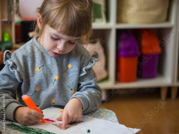 Fototapeta portrait of a little girl is drawn with a felt-tip pen. girl sits at the table and draws