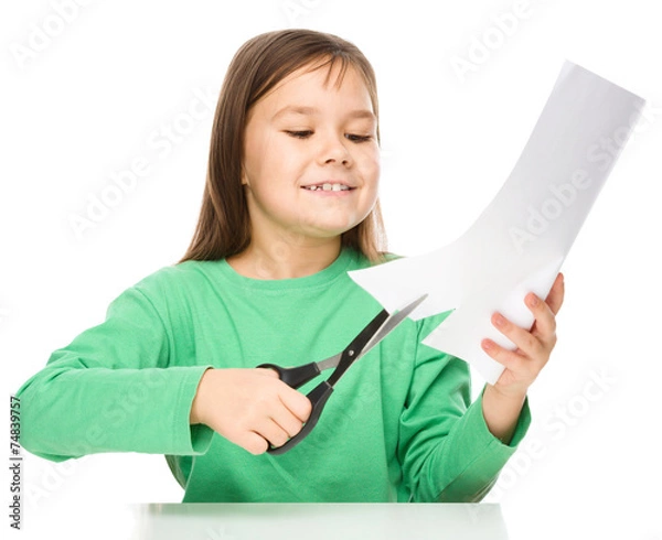 Fototapeta Little girl is cutting paper using scissors