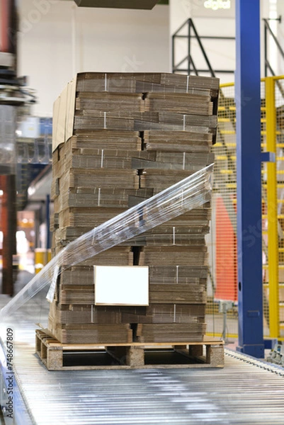 Fototapeta Freshly made manufactured cardboard boxes on a pallet getting shrink wrapped for transportation. Cardboard box storage and transport solution in a cardboard box factory.