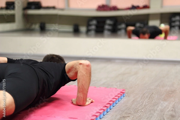 Obraz Man doing push-up on exercise mat in gym. Rear view.