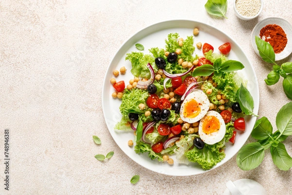 Fototapeta Soft-boiled egg Easter fresh vegetable salad with tomatoes, chickpea, olives, onion and green lettuce. Healthy food,  breakfast. Top view