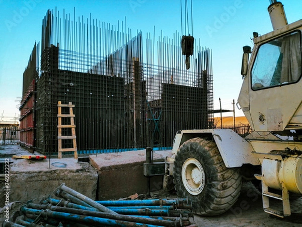 Fototapeta A construction site with a crane and a pile of construction materials. The crane is white and has a yellow cab. Scene is busy and active, with workers and machinery working together to build something
