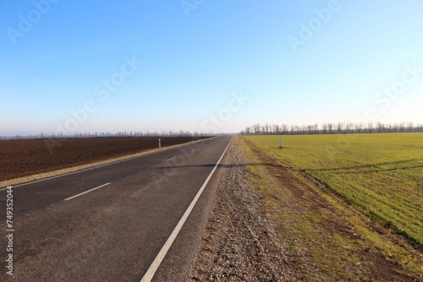 Obraz Asphalt road near agricultural fields and blue sky on a backround