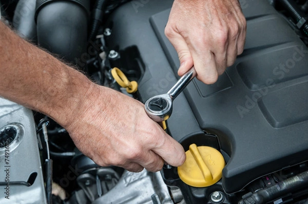 Fototapeta Mani che riparano un motore di automobile con una chiave