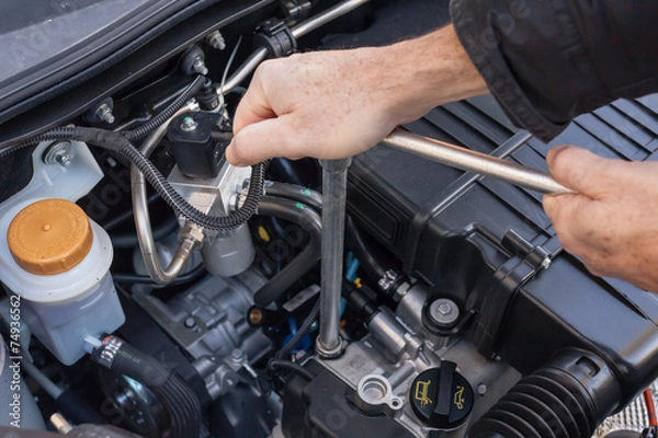 Fototapeta Mani che riparano um motore di automobile con una chiave