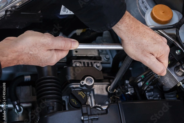 Fototapeta Mani che riparano um motore di automobile con una chiave