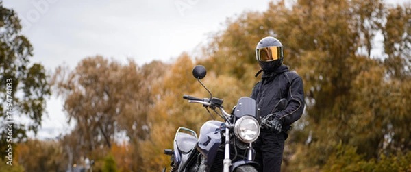 Fototapeta motorcyclist in a motorcycle jacket and tinted helmet with a classic motorcycle in nature. Stylish biker