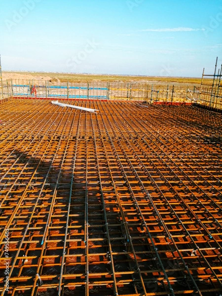 Fototapeta A construction site with a large area of metal mesh. The mesh is brown and the sky is blue