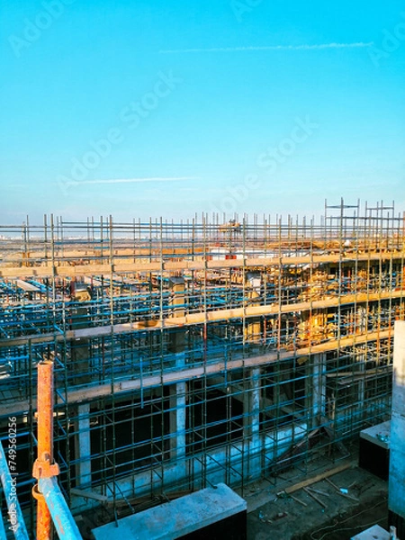 Fototapeta A construction site with scaffolding and a blue sky in the background. Scene is one of progress and hard work