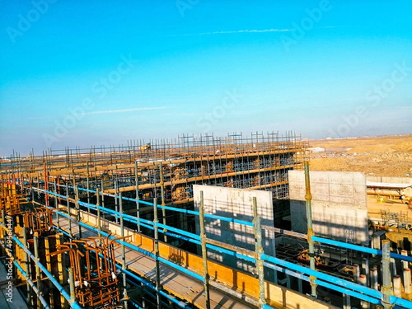 Fototapeta A construction site with scaffolding and a blue sky in the background. Scene is one of progress and hard work
