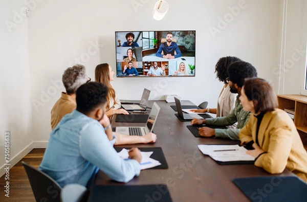 Obraz Team engaged in a virtual meeting with a display screen, showing both remote participants and in-person colleagues interacting seamlessly, integration of modern technology in collaborative workspaces