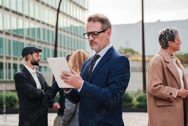 Fototapeta One mature business man using a digital tablet to work outside. Isolated mid adult executive employee browsing on internet with a touchpad at workplace. Successful male sending a email with a pad