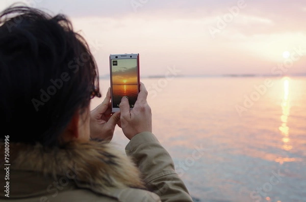 Obraz スマートフォンで初日の出を撮影する男性