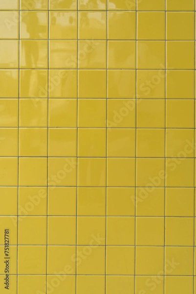 Fototapeta Section of wall covered with neatly arranged yellow tiles. Square-shaped material have uniform in size and color creating consistent and orderly look. Glossy surface