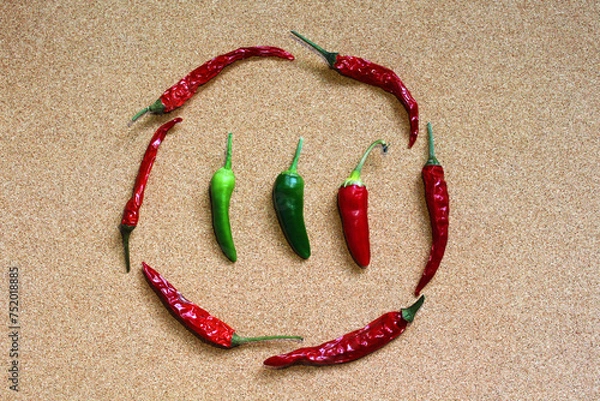 Fototapeta Fresh and dry chili peppers on cork background, top view. Composition of green and red capsicums. Unripe and ripe chili peppers in center of circle of dried peppers. Food photo