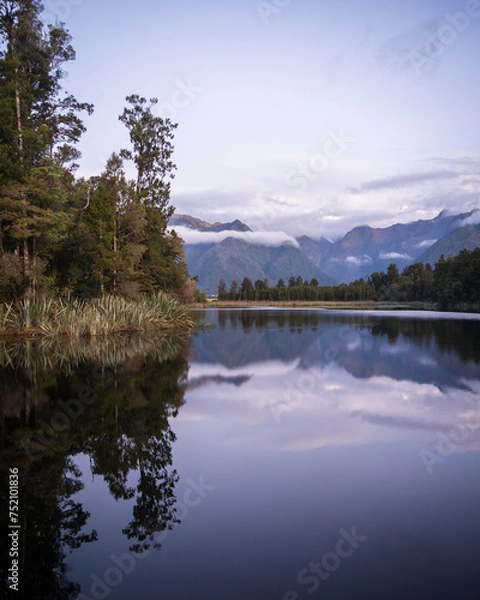 Fototapeta Beautiful lake surrounded by exotic forest and mountains in background during sunset, New Zealand