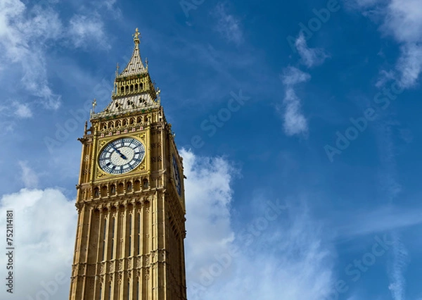 Fototapeta A low angle view of Big Ben against a blue sky with light clouds in Westminster, London, UK. 