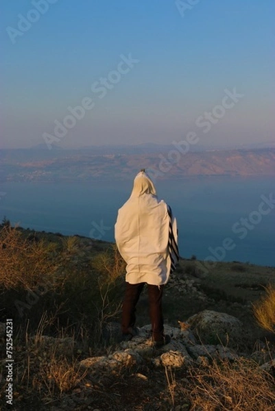 Fototapeta A Jewish man wraps himself in a tallit in prayer in nature