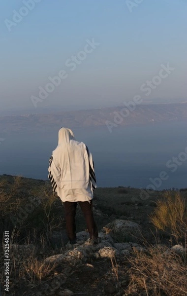 Fototapeta A Jewish man wraps himself in a tallit in prayer in nature