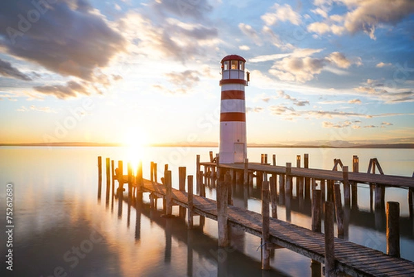 Fototapeta red and white lighthouse at sunset with clouds in the blue and orange sky