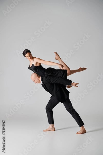 Fototapeta Graceful dance, young couple performing an acrobatic routine in a studio setting with grey backdrop
