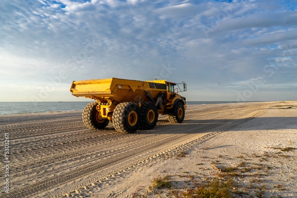 Fototapeta Articulated hauler mining type dump truck, in motion, carrying sand for a restoration project on a beach in the morning sun, Sanibel Island, Florida