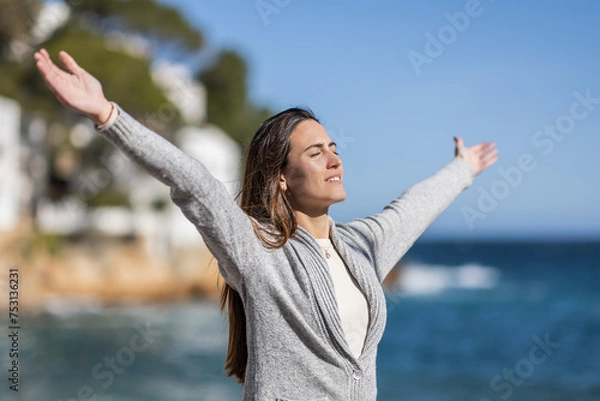 Fototapeta Smiling woman with arms outstretched on a beach, breathing fresh air.