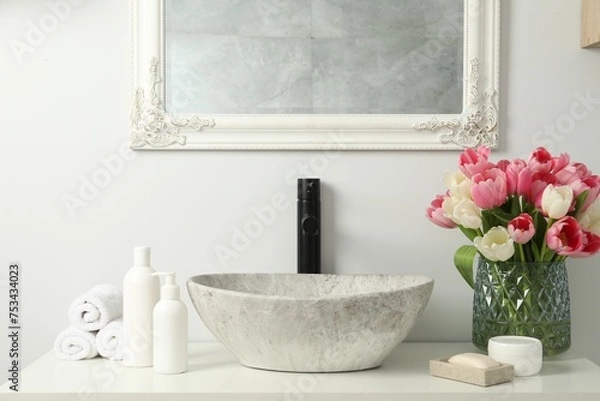 Fototapeta Vase with beautiful pink tulips and toiletries near sink in bathroom