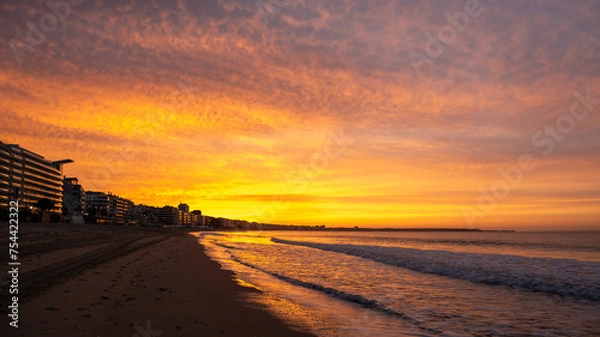 Fototapeta Amazing view of a fiery sunrise with multicolored clouds. Sea waves along the seashore at sunrise. Morning time. Ocean view. La Baule-Escoublac, France