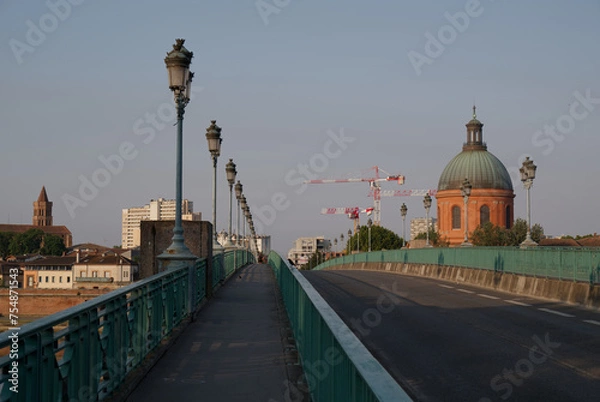 Obraz Pont Saint-Pierre Bridge in Toulouse, France. A serene early morning or evening scene of an empty bridge with ornate lamp posts leading towards a dome-capped building. In the background, construction.
