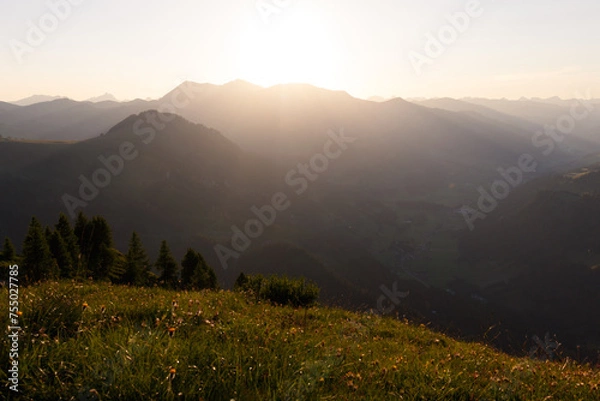 Fototapeta Sunset behind mountain range and green meadows in alpine region