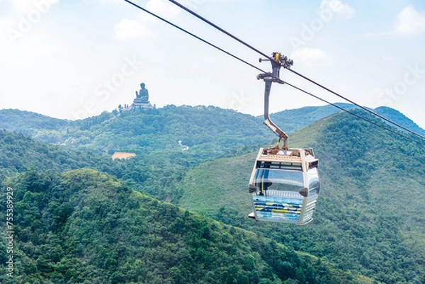 Fototapeta Overhead cable car riding through the mountain with Tian Tan Buddha statue on the far peak. It is one of transportations to the tourist attractions located at Ngong Ping, Lantau Island, in Hong Kong.