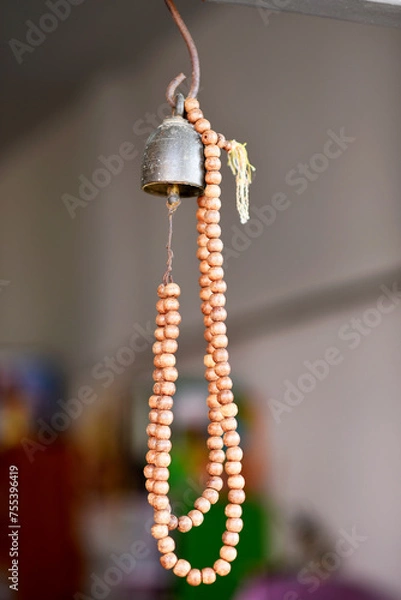 Fototapeta A brown wooden rosary is hung from a golden bronze bell on a blurred background.