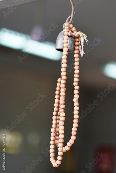 Fototapeta A brown wooden rosary is hung from a golden bronze bell on a blurred background.