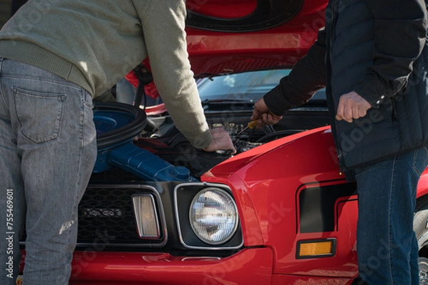 Fototapeta Concept of two men repairing the v8 engine of the old classic American first generation pony car. the man carries a screwdriver in his hand to adjust the carburetor and tune