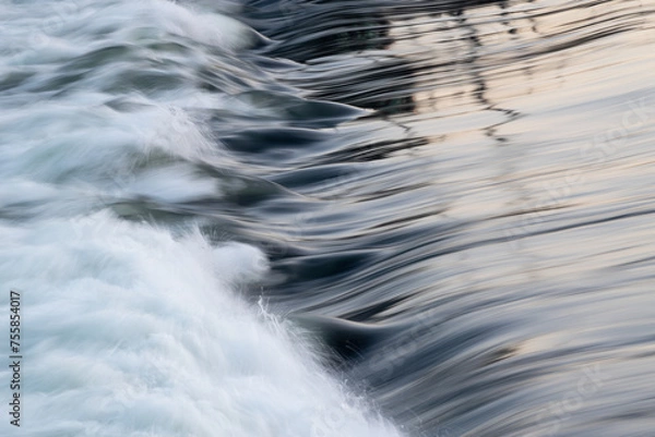 Fototapeta Rapid water flow over barrier with silky surface, river overflow over dam close up with splash and foam, abstract landscape pastel blue