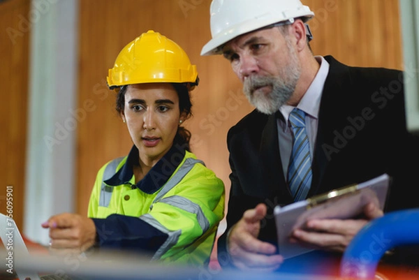 Fototapeta Two people are looking at a laptop, one of them is wearing a yellow jacket. Scene is serious and focused to machine controller board in factory.