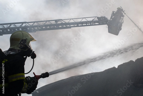 Fototapeta Firefighter extinguishes a fire of industrial hall with plastics with water from a hose
