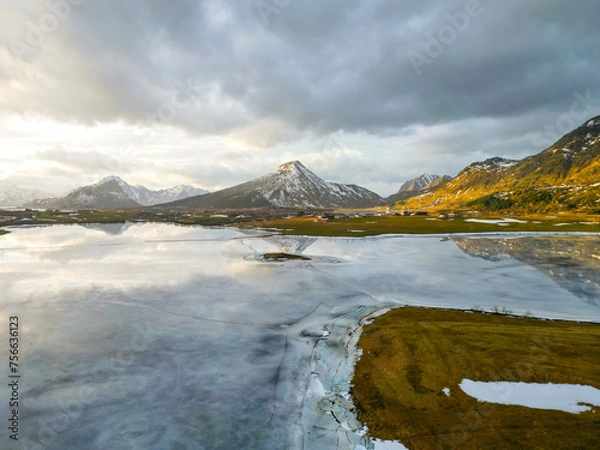 Fototapeta Panoramic view of beautiful white winter wonderland scenery with snowy mountain summits reflecting in crystal clear ice lake on a cold sunny day with sky and clouds. Norwegian fjords mountain.