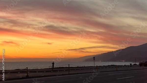 Fototapeta Anonymous, silhouetted person runs alongside the beach and Pacific Coast Highway at sunset, near Pacific Palisades, Los Angeles, California. Pacific Ocean and Santa Monica Mountains in background