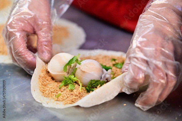 Fototapeta A vendor at the Ningxia Night Market in Taipei, Taiwan, assembles a peanut roll ice cream. The popular Taiwanese snack consists of a crepe, two scoops of ice cream, peanut brittle and coriander.