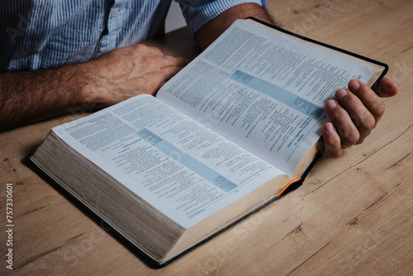 Fototapeta Man is reading the bible, holding with his hand the holy book, in a low-light environment